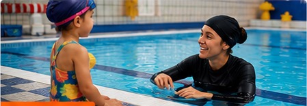 Swimming instructor talking with a child at the pool.